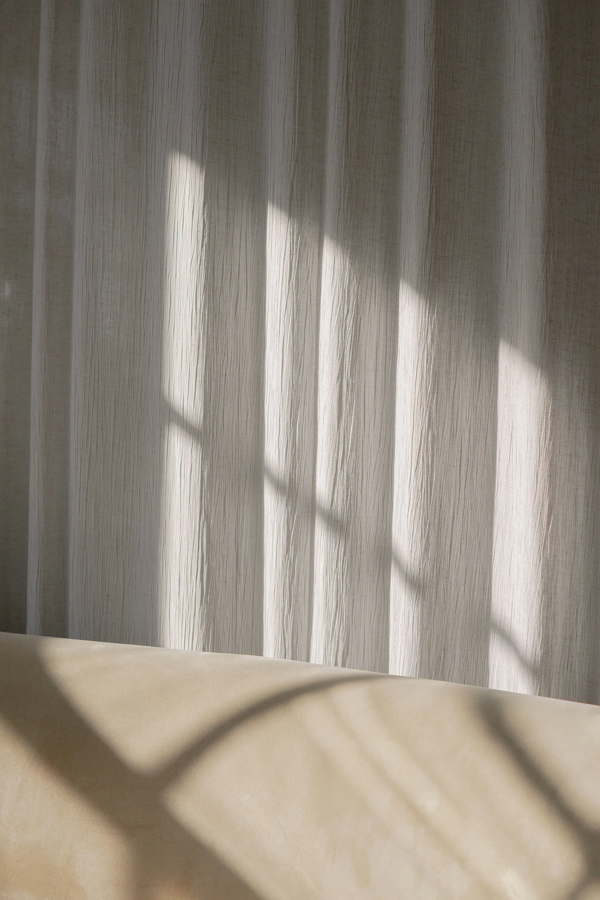 A linen curtain holding the soft striped shadow of a window.