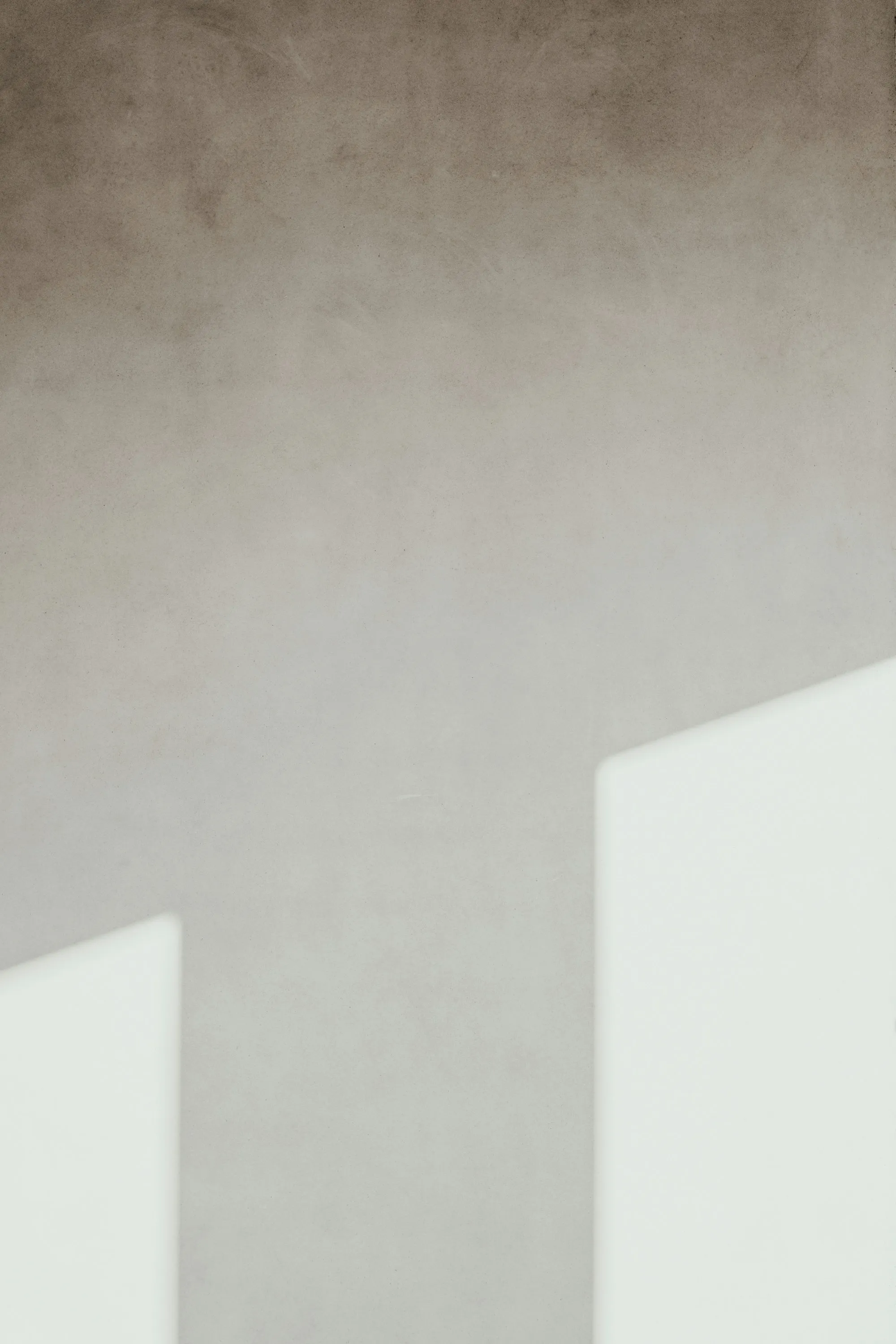 A soft plaster wall holding two hard rectangles of window light.