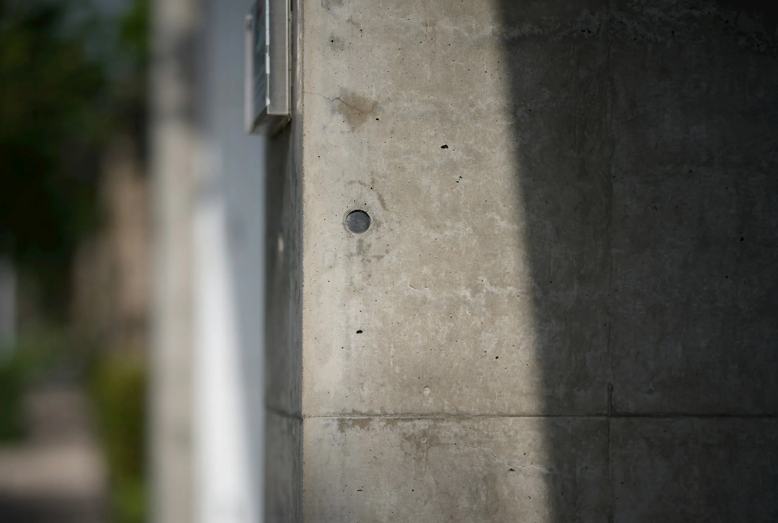 A concrete wall with a single dark shadow and a visible bolt.
